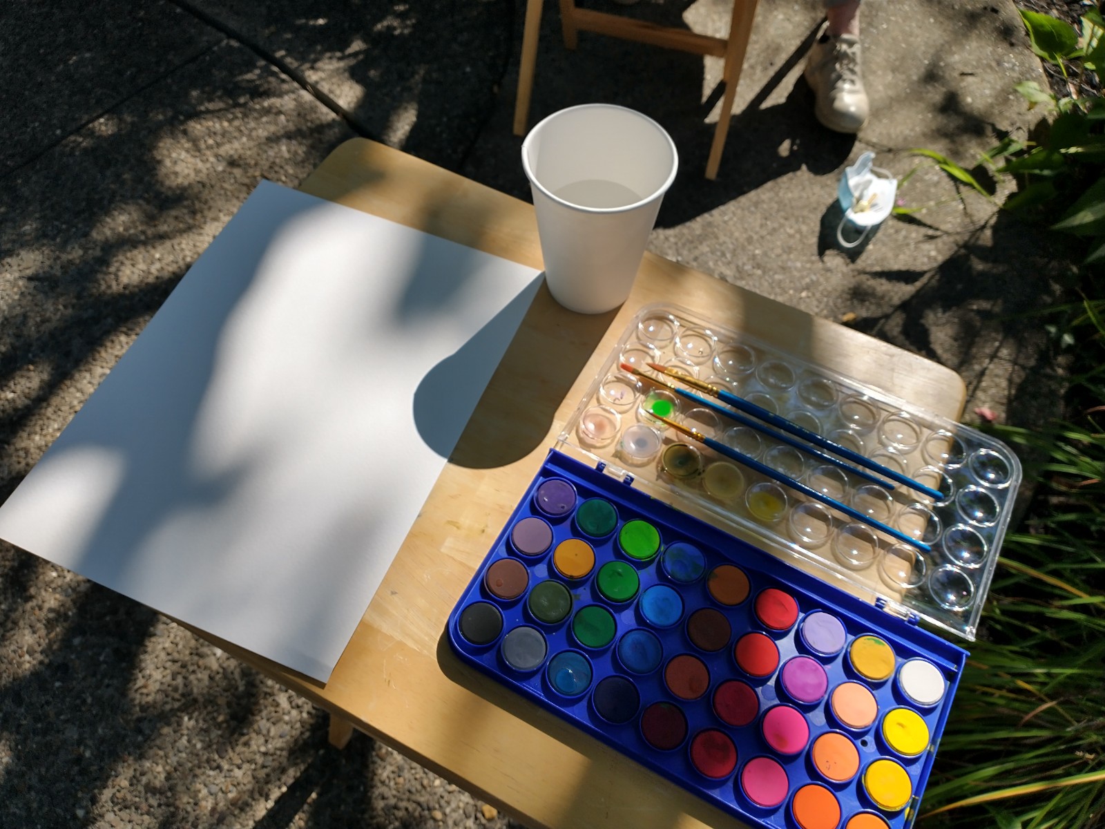 Tray table with a brand-new paint set, brush, watercolor paper, and a cup of water.