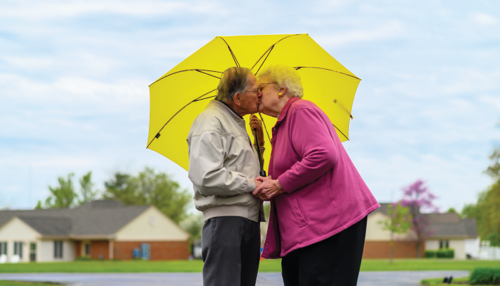 Otterbein Cridersville independent living couple kissing under yellow umbrella outdoors