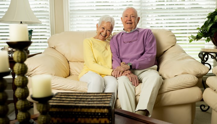 Otterbein SeniorLife couple sitting together on a sofa smiling and holding hands.