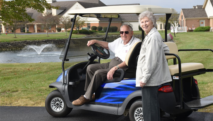 Smiling elderly couple by a golf cart in front of a pond at an senior independent living residence at Otterbein Cridersville